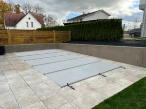 Hochwertige Poolabdeckung in Hellgrau schützt den Pool vor Verschmutzung und Wärmeverlust.