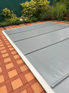 Mittelgraue Poolabdeckung mit verstärkten Alu-Stangen für maximalen Schutz und Energieeinsparung.