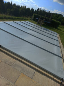 Wetterfeste Poolabdeckung in Mittelgrau mit Aluminiumverstärkung auf einer Steinfliese.