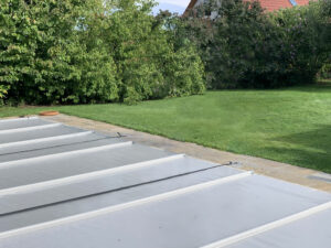 Mittelgraue Poolabdeckung mit Verstärkung auf einer Terrasse im Garten.