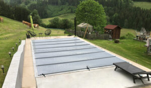 Mittelgraue Poolabdeckung auf einer erhöhten Terrasse mit Blick auf eine grüne Landschaft und weidende Kühe.