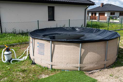 Ein runder Aufstellpool mit schwarzer Abdeckplane im Garten, geschützt vor Schmutz und Laub.
