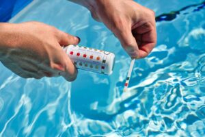 Person prüft den pH-Wert im Pool mit einem Teststreifen zur Wasseranalyse